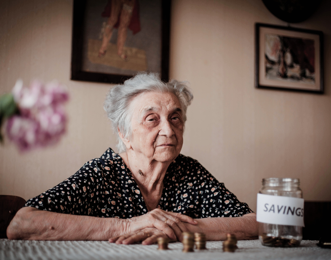 Mujer mayor sentada junto a una mesa en la que vemos sus ahorros