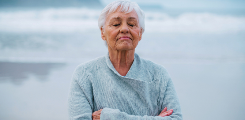 Imagen de una mujer mayor meditando frente al mar