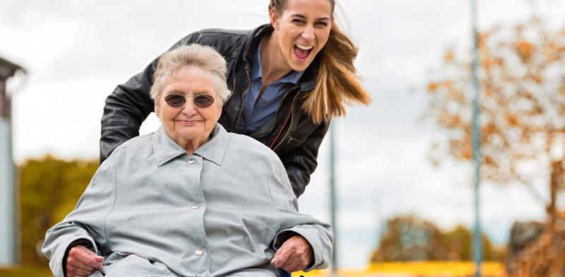 Mujer joven empuja la silla de ruedas de una mujer mayor