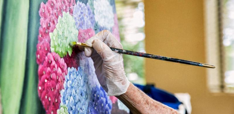 Mano con un pincel pintando un lienzo de unas flores